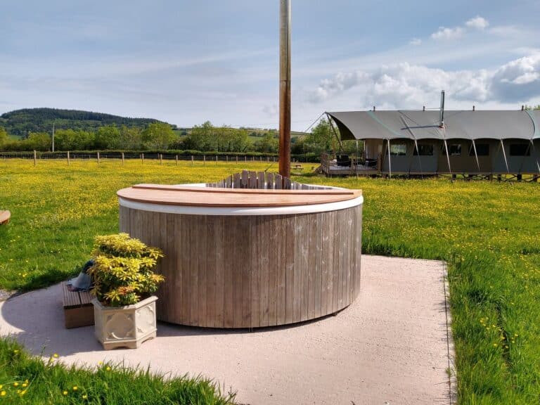 Wood-fired hot tub in a buttercup meadow with a safari tent behind, Somerset