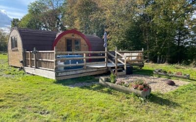 Pod at Little Halden Farm seen across the grass, with its hot tub on the decking and raised flower beds alongside