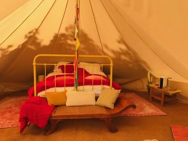 Bell tent interior with iron bed, red blankets and rugs