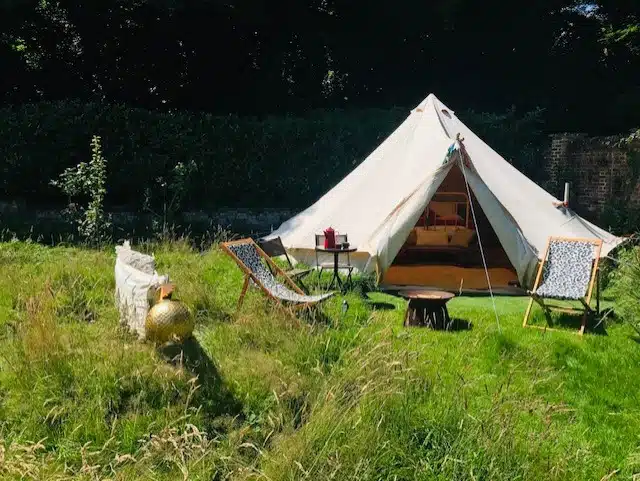 Bell tent with deckchairs and a fire pit in long grass