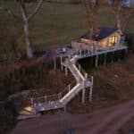 Elevated treehouse cabin with lit staircase at dusk, Oaklands, Powys