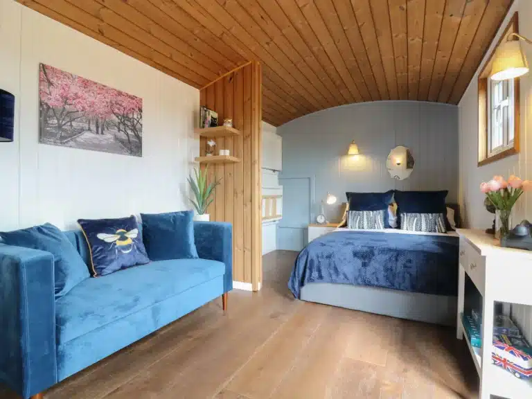 Bed and sofa in a Shepherds Hut at Lodeside Glamping Cambridgeshire