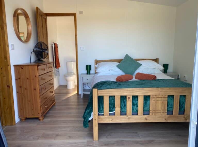 Cabin bedroom with a pine double bed, teal and orange cushions and a chest of drawers