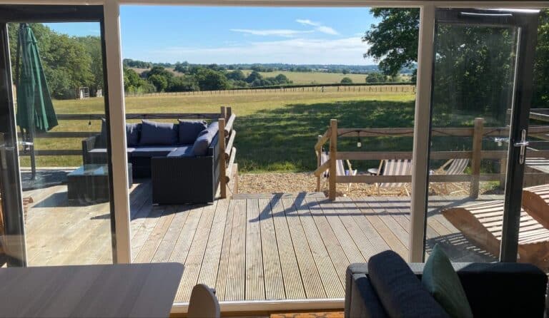 View from inside the cabin through glass doors to the decked terrace and countryside