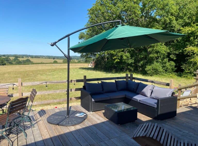 Decked terrace with a corner rattan sofa and green parasol overlooking the Kent fields