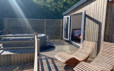 A hot tub and wooden sun loungers on a deck behind a privacy screen in the sunshine
