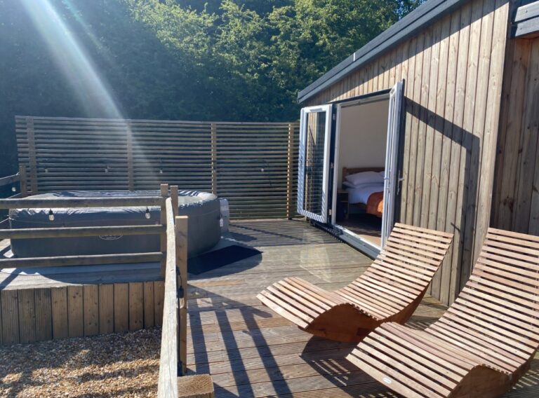 A hot tub and wooden sun loungers on a deck behind a privacy screen in the sunshine