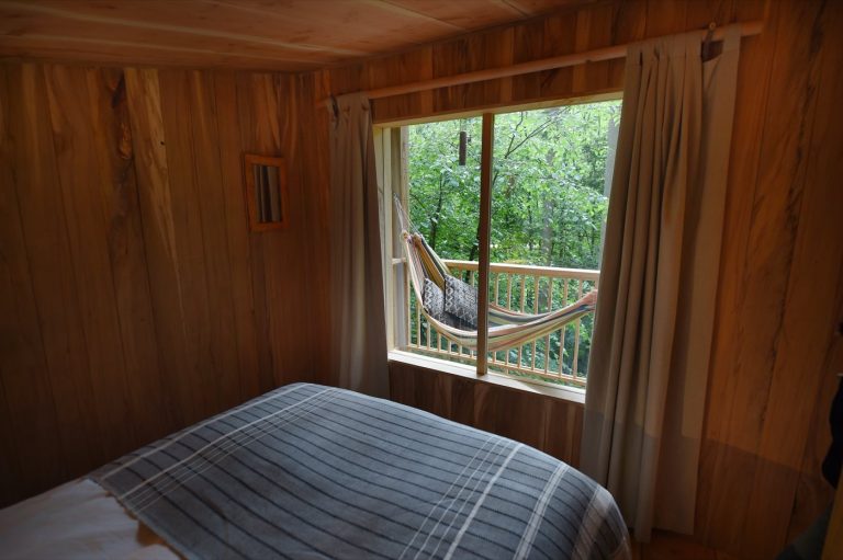 Double bed beside the large window of the Treetop Cabin, looking out into the woodland