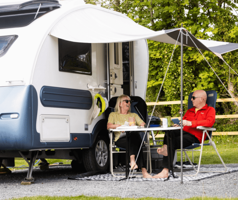 Couple sat outside their touring caravan, enjoying the peace and nature at Meadow Falls