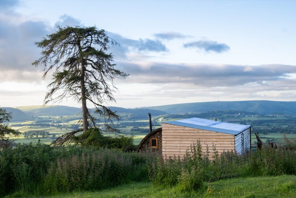 Timber glamping pod on a Powys hillside at golden hour above the valley