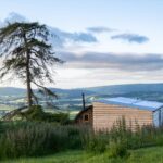 Timber glamping pod on a Powys hillside at golden hour above the valley