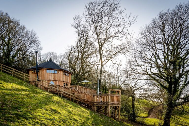 Round timber treehouse with boardwalk and decking on a wooded hillside, Devon