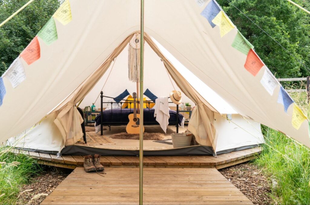 Bell tent interior with iron bed, sheepskins and a guitar, prayer flags outside