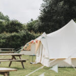 A bell tent with a picnic bench and its door open in a field