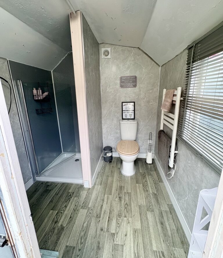 Private shower room in a service cabin at Glamp and Tipple with a corner shower, WC, heated towel rail and marble-effect walls