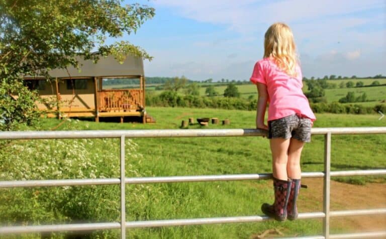 Girl on a gate overlooking a field with safari tent at Village Farm Hideaway Leicestershire