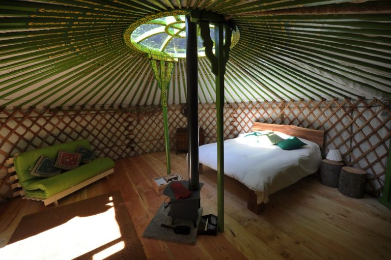 Inside a 19ft yurt at Redwood Valley, with log burner, bed and the crown wheel above