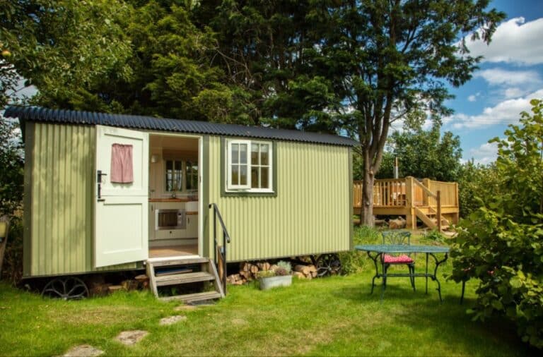 Sage-green shepherd's hut with its door open and decking, on the lawn at Abbey Farm in the Chilterns