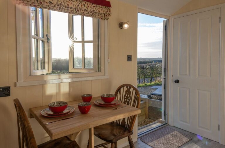 Dining table by open doors leading onto the terrace and countryside view at Abbey Farm
