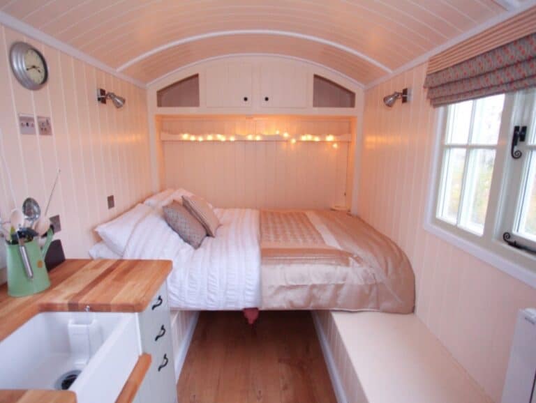 Double bed with fairy lights under the curved roof of a shepherd's hut at Abbey Farm