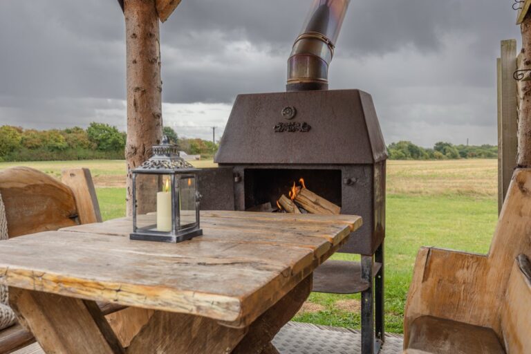 Outdoor wood burner and rustic dining table on the stoep at Tinywood One, looking over open fields
