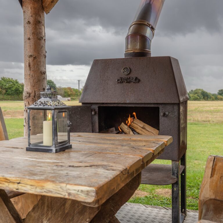 Lit outdoor wood burner beside the table at Tinywood One on an autumn evening